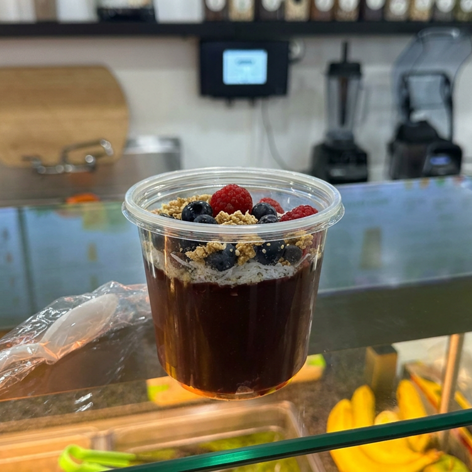 Clear cup of dark dessert topped with granola, blueberries, and raspberries on a café counter.