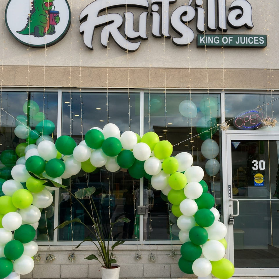 Frusli King of Juices storefront decorated with a green, white, and lime balloon arch around the entrance.