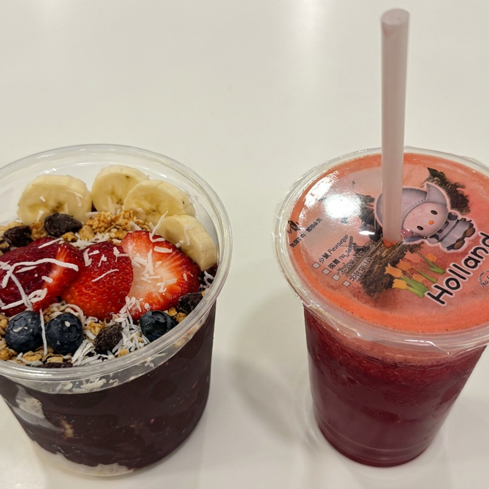 Acai bowl topped with strawberries, bananas, blueberries, granola, coconut, and chocolate beside a red fruit smoothie.